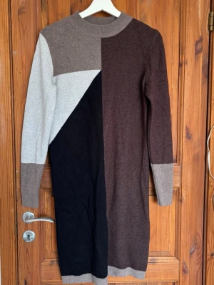 Flerfärgad klänning  - Snygg lång stickad klänning i blockfärger med svart, brun, beige och grå. Klänningen har lång ärm och hög hals, perfekt för kyligare dagar. Mjuk och bekväm med en rak passform och ribbade muddar vid ärmslut och nederkant. Har använt den 2 gånger så superfint skick💖🌸