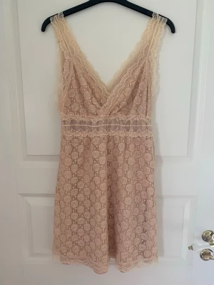 Beige spetsklänning med v-ringning - Söt kort beige klänning i spets med v-ringad omlott framtill och breda axelband. Klänningen har ett fint cirkelmönster i spetsen och dekorativ spetskant längs urringningen och midjan. Perfekt för sommarens alla tillfällen. Kolla gärna mina andra annonser❗️