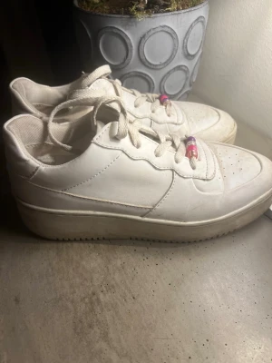 Vita chunky sneakers med pärldetalj - Stilrena vita sneakers med chunky sula och perforerade detaljer på tån. Skorna har vita skosnören med färgglada pärlor som accent. Klassisk låg modell som passar till det mesta. 