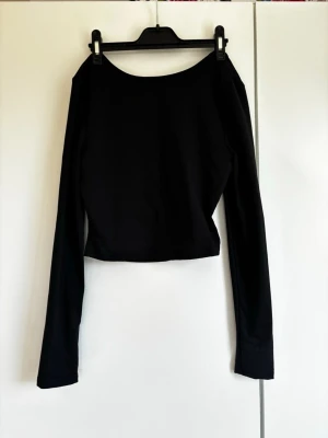 Svart långärmad croppad topp - Säljer en svart långärmad croppad topp med öppen rygg. Toppen har en enkel och stilren design med rund halsringning och är tillverkad i ett mjukt stretchigt material, perfekt för att matcha med höga jeans eller kjol. Som ej är använd. 