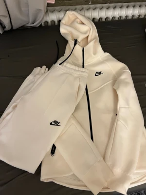 Vit Nike hoodie med dragkedja och huva - Säljer en stilren vit hoodie från Nike med svart dragkedja och huva. Hoodien har Nike-logga på bröstet och praktiska fickor med dragkedja. Tillverkad i mjukt material som passar perfekt för en avslappnad look. Den är helt ny aldrig använt