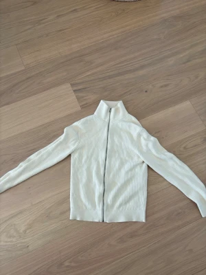 Vit ribbad tröja med dragkedja - Snygg vit ribbad tröja med hög krage och dragkedja framtill. Perfekt till lager på lager och enkel att styla till olika outfits. Långärmad modell i mjukt material som ger en clean och fräsch look.