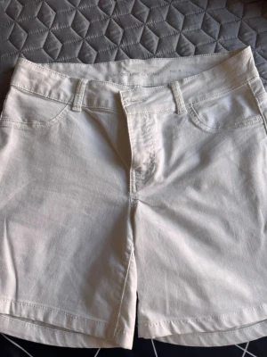 Vita denimshorts från Jacqueline de Yong - Snygga vita denimshorts från Jacqueline de Yong med klassisk femficksmodell, bälteshällor och knappgylf. Perfekta för sommaren och har en enkel, clean look som passar till allt. Materialet är mjuk bomull med en skön passform.