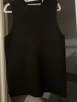 Svart stickad väst - Säljer en svart stickad väst i ribbat material. Västen är ärmlös med rund halsringning och har en rak, avslappnad passform. Perfekt att styla över en skjorta eller t-shirt för en trendig lager-på-lager-look.