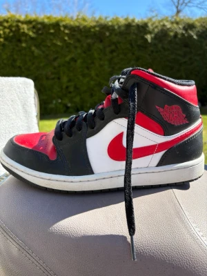 Nike Air Jordan 1 High röd/svart/vit - Säljer en Nike Air Jordan 1 High med klassisk färgkombination i rött, svart och vitt. Skon har svart snörning, röd swoosh och Air Jordan-logga på sidan. Tillverkad i läder med vadderad krage för extra komfort. Perfekt för dig som gillar streetwear och sneakerskultur. Pris kan diskuteras!