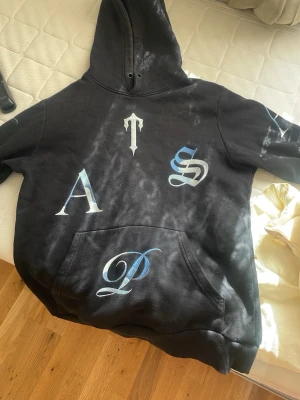 Svart hoodie med stora bokstäver - Svart trapstar hoodie i storlek M. Den är använd några gånger men är i bra skick utan några skador. Vill inte ha den längre då jag tappat intresse för stilen den är äkta utan skador