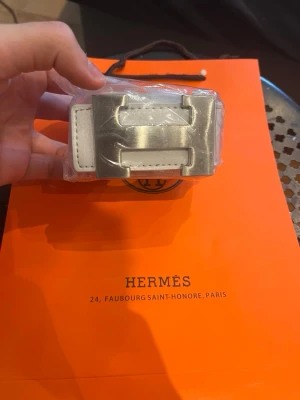 Vitt Hermès bälte med silverdetaljer - Snyggt vitt bälte från Hermès med ikoniskt H-spänne i silverfärgad metall. Bältet har stilrena sömmar och klassisk design som lyfter vilken outfit som helst. Perfekt accessoar för dig som gillar exklusiva detaljer och tidlös stil.