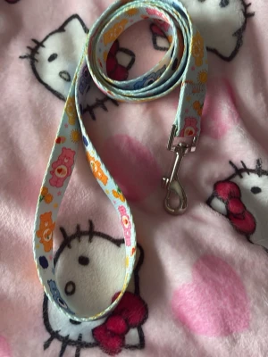 Söt Care Bears hundkoppel - Färgglatt hundkoppel med Care Bears-motiv på ljusblå botten och små solar och hjärtan. Kopplet har en metallkrok i silverfärg och är gjort av slitstarkt tyg. Perfekt för dig som vill ha något gulligt till din hund. ✨liten gåva vid varje köp!