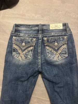 Low waist jeans  - Säljer ett par blå jeans från Miss Me med snygga slitningar och broderade bakfickor med glittriga detaljer. Jeansen har raka ben och klassisk femficksmodell. Perfekta för dig som vill ha ett par jeans med extra attityd och detaljer. Endast använt 1 gång! 