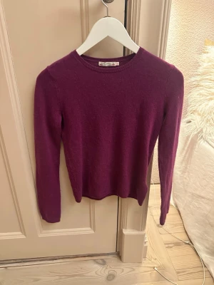 Lila stickad tröja från Bonpoint - Säljer en lila stickad tröja från Bonpoint med rund halsringning och långa ärmar. Tröjan har en enkel och stilren design, perfekt att matcha med olika outfits. Materialet känns mjukt och bekvämt mot huden.