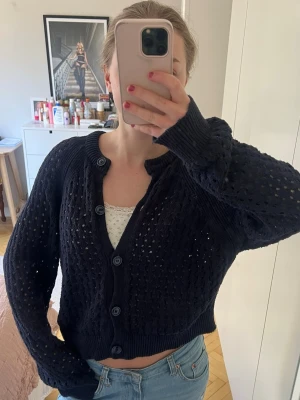 Marinblå kofta med knappar - Snygg marinblå stickad kofta med stora knappar framtill och rund halsringning. Koftan har ett genombrutet mönster och ribbade muddar vid ärmslut och nederkant. Perfekt att slänga över ett linne eller t-shirt för en chill look.