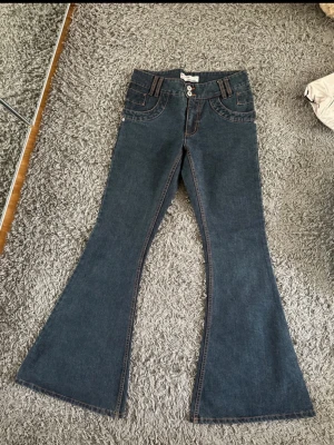 Mörkblå jeans från ICHI - Säljer ett par mörkblå jeans från ICHI med bootcut ben och dubbla knappar i midjan. Jeansen har dekorativa sömmar i kontrastfärg och flera fickor fram. Klassisk denimlook som passar till det mesta.