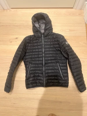 Svart dunjacka med huva från Colmar - LIGHT DOWN JACKET WITH HOOD - Säljer en svart dunjacka från Colmar med huva och två dragkedjeförsedda fickor framtill. Jackan har quiltad design och Colmar-logga på ärmen. Jackan är i bra skick utöver en litet hål på ena ärmen, där det är lagat med en lag lapp. Därav billigt pris. Tveka inte på att höra av er!