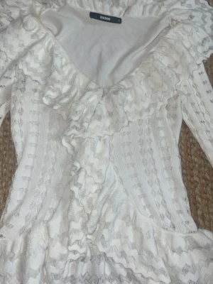 Vit spetsklänning med volanger BikBok - Romantisk vit spetsklänning från BikBok med långa ärmar och v-ringning. Klänningen har volangdetaljer längs ringningen och framtill, samt ett vackert spetsmönster som ger en feminin look.