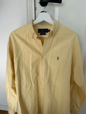 Gul skjorta från Ralph Lauren - Hjälper min bror att sälja. Klassisk gul skjorta från Ralph Lauren med button-down krage och broderad logga på bröstet. I storlek M. I bra skick. Säljs för 280 kr.