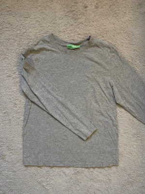 Grå långärmad tröja från JJXX - En enkel och stilren grå långärmad tröja från JJXX. Tröjan har rund halsringning och är tillverkad i mjuk bomull, perfekt för en avslappnad look. Passar till det mesta och är lätt att matcha med andra plagg.