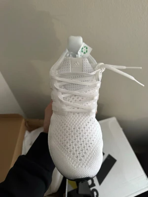 Vita Adidas Ultraboost sneakers - Fräscha helvita Adidas Ultraboost sneakers med stickad ovandel och klassiska tre ränder på sidan. Skon har en bekväm Boost-sula och ventilerande meshmaterial för extra komfort. Perfekt för dig som gillar stilrena och sportiga sneakers.