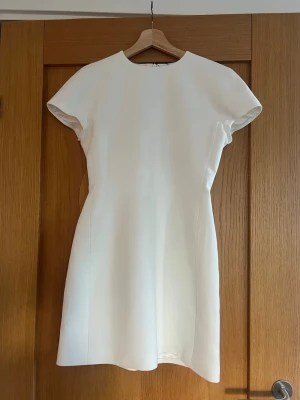 Vit kortärmad studentklänning från Zara, stl S - Stilren vit klänning från Zara med korta ärmar och rund halsringning. Klänningen har en enkel, figurnära passform och är tillverkad i ett mjukt tyg som ger en elegant look. Perfekt för studenten👩‍🎓🥳! Helt ny med prislapp kvar! 