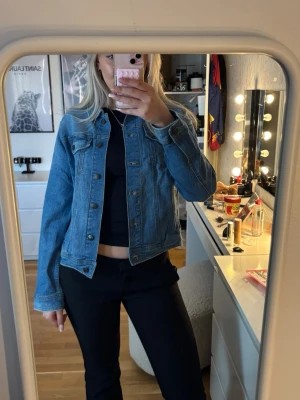 Klassisk blå jeansjacka - Snygg blå jeansjacka i klassisk modell med knappar framtill och två bröstfickor. Jackan har raka ärmar och en tidlös passform som funkar till det mesta. Perfekt att slänga över en t-shirt eller hoodie för en cool look.