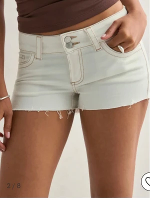 Vita denimshorts - Säljer ett par vita denimshorts med rå kant och kontrastsömmar. Shortsen har låg midja, dubbla knappar och klassiska fickor fram och bak. Snygg detalj med broderad bakficka. Perfekta för varma dagar! Helt oanvända!