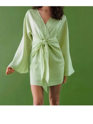 Limegrön omlottklänning med knytband från Gina Tricot - Perfekt till sommarfesten! Kort klänning i fin limegrön färg med omlottdesign och knyt i midjan. Materialet har en lätt glans och känns mjukt mot huden. Endast testad men aldrig använd. 