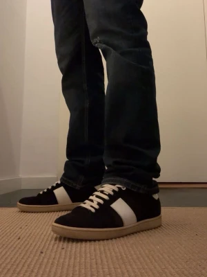 Svarta Saint Laurent sneakers i mocka - Snygga svarta sneakers från Saint Laurent i mocka med vita detaljer och vita skosnören. Klassisk låg modell med vit sula och diskret logga på plösen. Perfekta för dig som gillar stilrena och tidlösa sneakers.