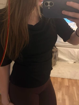 Svart topp med draperad hals - Svart topp med draperad halsringning och halvlånga ärmar. Snygg och enkel modell som sitter figurnära. Från märket STOCKH LM. Använd fåtal gånger.