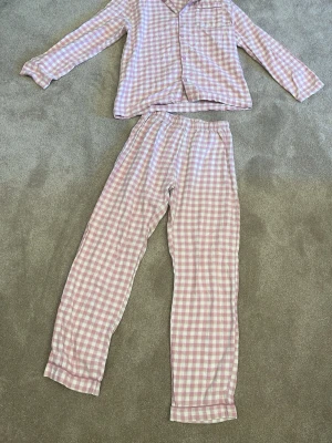 Rutig pyjamas i rosa och vitt - Mysig tvådelad pyjamas med långärmad skjorta och byxor i rosa och vitt rutigt mönster. Skjortan har knappstängning och en bröstficka, byxorna har resår midjan. Har sytt igen ett hål men tycker bara det spycar till de hela lite. 