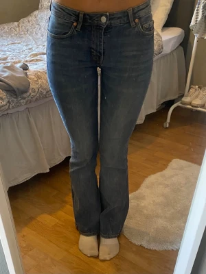 Blå bootcut jeans med hög midja - Snygga blå bootcut jeans med hög midja och klassisk femficksdesign. Jeansen har en lätt tvättad look och sitter tajt över låren för att sedan släppa ut vid vaden. Perfekta för dig som gillar en retro vibe och vill ha ett par jeans som sticker ut lite extra. 