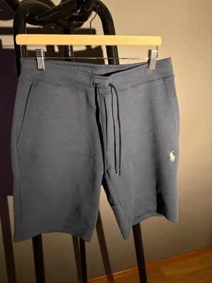 Mörkblå shorts från Polo Ralph Lauren - Mörkblå shorts från Polo Ralph Lauren med klassisk broderad logga på benet. Modellen har snörning i midjan och två sidofickor. Perfekta för en avslappnad stil och tillverkade i mjuk bomull för extra komfort.