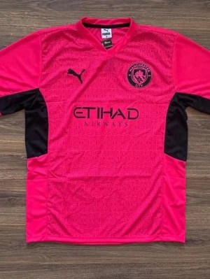 Manchester City rosa matchtröja Puma - Snygg rosa Manchester City matchtröja från Puma med svarta detaljer på sidorna och ärmarna. Tröjan har klubbmärke och Puma-logga på bröstet samt Etihad Airways tryckt på framsidan. Perfekt för dig som älskar fotboll och vill sticka ut på planen.