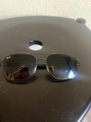 Svarta Raybans - Snygga solglasögon i klassisk pilotmodell med svarta bågar och blå spegelglas. Metallbågarna ger en stilren look och glasen har en cool reflektion. Perfekta för dig som vill ha en tidlös accessoar med edge.