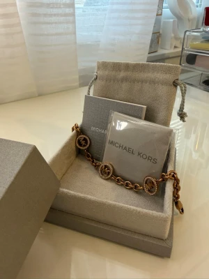 armband från Michael Kors - Snyggt armband från Michael Kors i roseguldfärgad metall med kedjelänk och runda berlocker med MK-logga. Perfekt accessoar för dig som gillar stilrena detaljer och exklusiv känsla. Kommer i originalask med tillhörande påse och kort. 