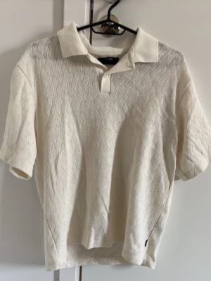 Vit stickad polotopp från Jack & Jones - Säljer en vit stickad polotopp från Jack & Jones. Toppen har korta ärmar, krage och diskret strukturmönster i tyget. Perfekt till jeans eller shorts för en clean och stilren look.