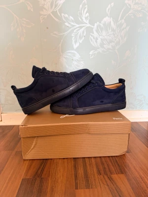 Mörkblå sneakers från Louboutin - Stilrena mörkblå sneakers från Christian Louboutin i mocka med matchande mörkblå sula och snörning. Klassisk låg modell med diskret design och mjukt innerfoder. Perfekta för dig som gillar minimalistisk och lyxig stil.