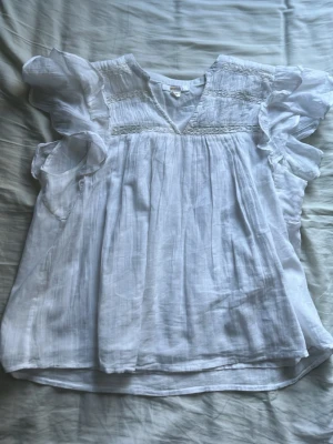 Vit blus med volangärmar - Supersöt vit blus i tunn och luftig bomull med volangärmar och smockdetaljer upptill. Blusen har v-ringning och ett lätt, flowy fall som ger en romantisk känsla. Jag säljer för den inte passar mig. Den är 158-164 men tror också den skulle funka för någon med Xs eller S.