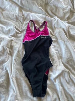 Svart och cerise baddräkt från Stenoduto - Sportig baddräkt i svart och cerise från Stenoduto. Modellen har brottarrygg och kontrasterande vita sömmar. Tillverkad i stretchigt material som passar perfekt för simning och träning. 