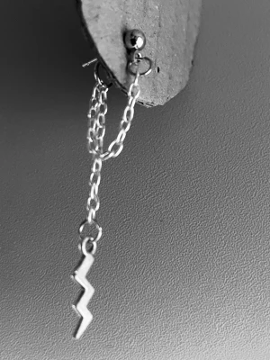 By prisförslag- 1 st Silverörhänge med blixt och kedja - coolt silverfärgat örhänge med en blixtformad hängande detalj och dubbla kedjor. Örhänget har en rund plupp upptill och är tillverkat i metall. Perfekt för dig som gillar edgy och unik stil.