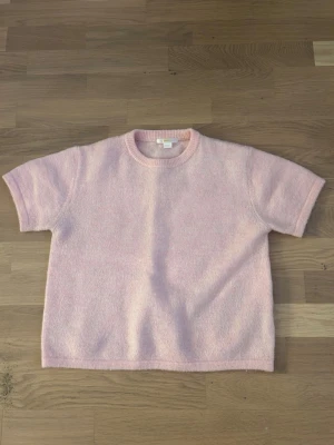 Ljusrosa stickad kortärmad topp - Superfin ljusrosa stickad topp med rund hals och korta ärmar. Mjuk och skön, perfekt för lager-på-lager eller som den är. Enkel och stilren design som passar till mycket.