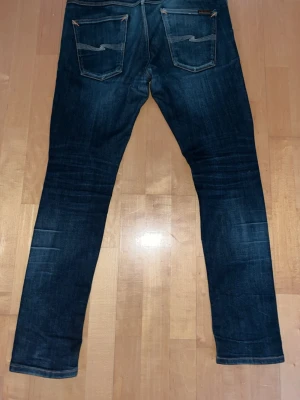 Mörkblå jeans från Nudie Jeans - Säljer ett par mörkblå jeans från Nudie Jeans i modellen lean dean. Snygg vit söm på bakfickorna, hör av dig vid frågor och funderingar!!!🛑Finns en del på baksidan där tyget är väldigt tunnt. Inte hål men slitet