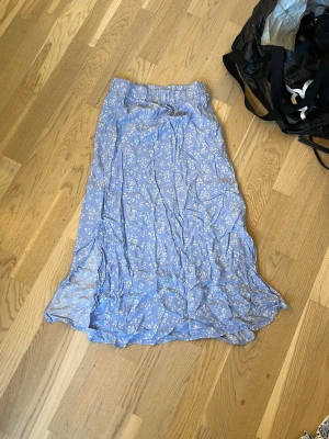 Blommig blå långkjol från lager 157 - Söt blå långkjol från Lager 157 med vitt blommönster och resår i midjan. Kjolen har en flowy passform och är perfekt för vår och sommar. Lätt och luftig i materialet, vilket gör den bekväm att bära hela dagen.