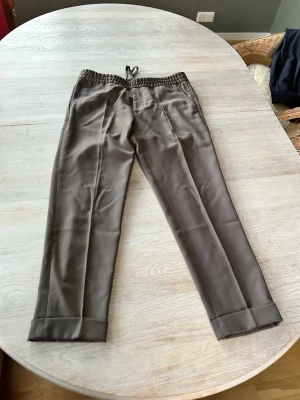 Fillippa k byxor - Stilrena svarta kostymbyxor med resår i midjan och raka ben. Byxorna har pressveck framtill och uppvikta benslut för en modern look. Perfekta för dig som vill ha en dressad men avslappnad stil.