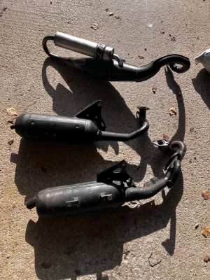 Tre avgassystem till moped - Säljer tre avgassystem till moped, två är mattsvarta och ett har en silverfärgad ljuddämpare. Alla har böjda rör och fästen för montering. Perfekt för dig som vill byta eller uppgradera din mopeds ljud och prestanda.