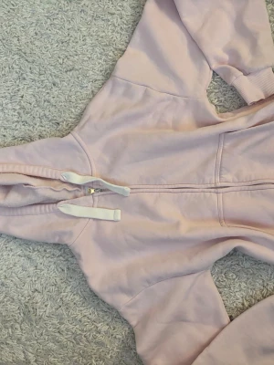 Ljusrosa hoodie med dragkedja - Mysig ljusrosa hoodie med dragkedja framtill och vita snören i huvan. Hoodien har ribbade muddar vid ärmsluten och en klassisk känguruficka. Från gina tricot.storlek xs.
