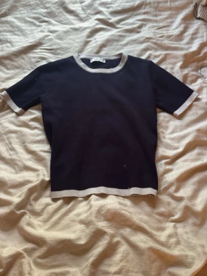 Mörkblå topp med vita detaljer från Zara - En svart kortärmad topp från Zara med vita ribbade kanter vid hals💕, ärmslut och nederkant. Toppen har en liten slit längst ner på toppen i varje hörn.. Perfekt för en stilren outfit💕använt fåtal gånger och frakt ingår, 35kr