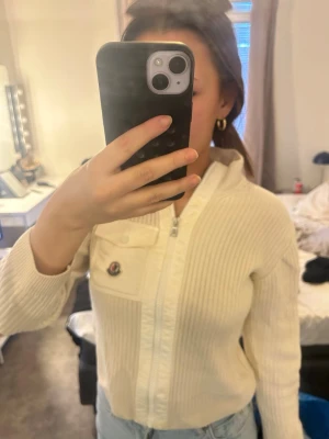 Vit ribbad zip-kofta från Moncler - Säljer en vit ribbad kofta från Moncler med dragkedja framtill och huva. Koftan har ett diskret Moncler-emblem på bröstet och en bröstficka med knapp. Materialet är mjukt och stretchigt, perfekt för en chill look. Som ni ser på bild 2 har den gått sönder en person som kan sy så är de inga problem pris går diskutera 