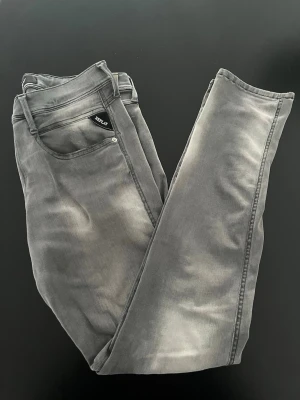 Grå jeans från Replay - Snygga grå jeans från Replay med slitna detaljer och klassisk femficksdesign. Jeansen har raka ben och coola broderier på bakfickorna. Materialet är mjukt och stretchigt för extra komfort. Perfekt för dig som gillar en avslappnad och trendig look.