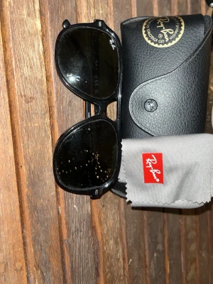 Svarta Ray-Ban solglasögon barn - Snygga svarta solglasögon från Ray-Ban med klassisk pilotform. Bågarna är i svart plast och glasen är mörka. Kommer med originalfodral och putsduk med Ray-Ban-logga. Perfekta för dig som vill ha en tidlös look. Dom är i barnstorlek och borde passa barn i åldern 4-13. Säljes och mötes i Stockholm.