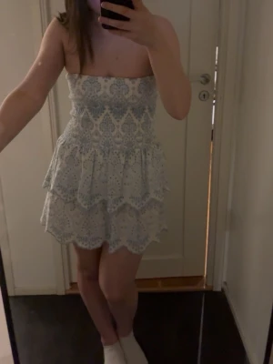 Strapless vit klänning med blått mönster - Säljer en kort, axelbandslös klänning i vitt med blått broderat mönster. En perfekt sommarklänning. Klänningen är i storlek M men passar som en S nästan XS. Jag har bara använt  en gång 💕