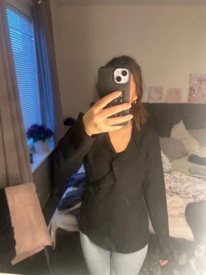 Svart omlottblus med knyt - Stilren svart omlottblus med knyt i sidan och v-ringad hals. Långa ärmar och en lätt figurnära passform gör den enkel att matcha till olika looks. Perfekt för dig som gillar en klassisk men trendig stil.
